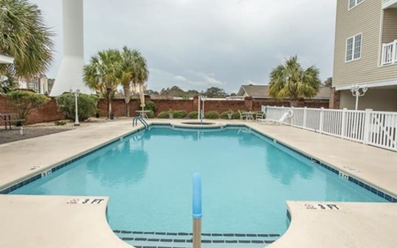 Rectangular swimming pool with clear blue water, surrounded by concrete deck, palm trees, and multi-story residential building