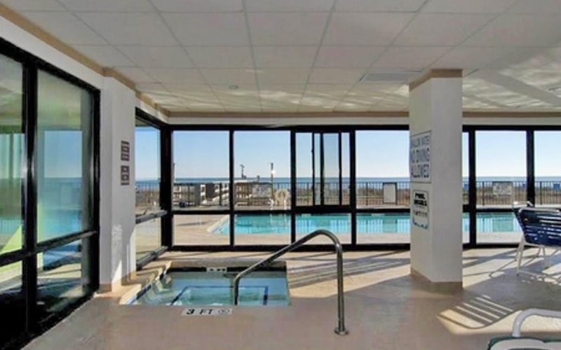 Indoor pool area with large windows overlooking outdoor swimming pool and ocean view