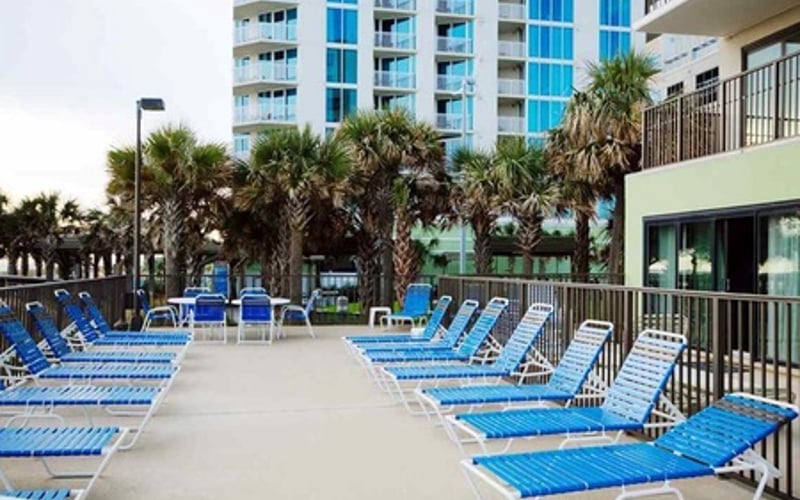 Pool deck with blue lounge chairs, palm trees, and beachfront condominium towers in background