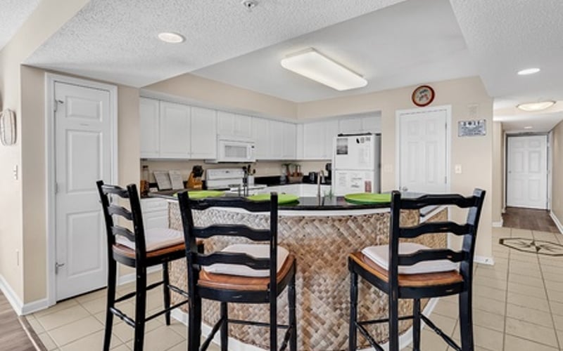Kitchen with white cabinetry, island with bar seating, and black ladder-back chairs