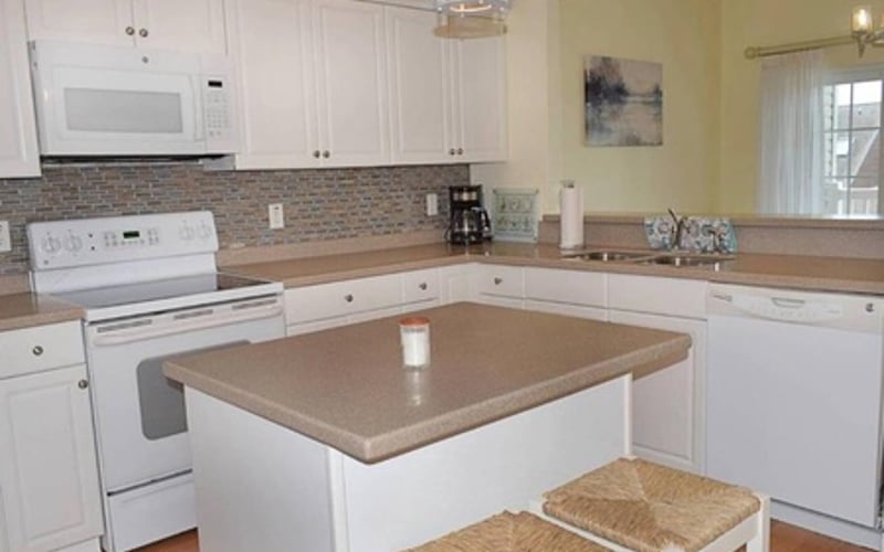 Kitchen with white cabinets, brown countertops, brick backsplash, and central island with seating