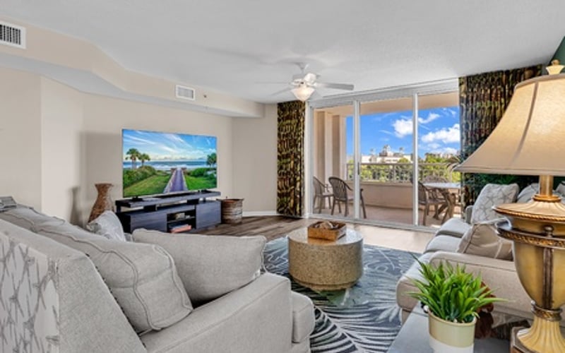 Modern condo living room with gray sofa, wall-mounted TV, and balcony overlooking city skyline
