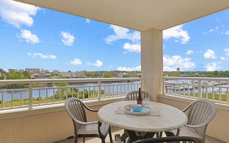 Balcony with round table and chairs overlooking waterway and distant buildings under blue sky