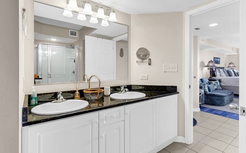 Bathroom with white vanity, dual sinks, black countertop, and large mirror with lighting