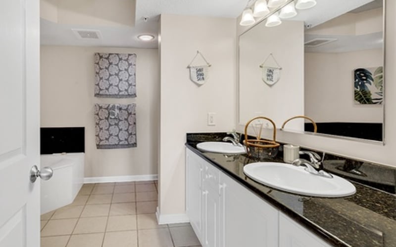 Modern bathroom with dual vanity, dark granite countertop, white cabinetry, and large mirror with overhead lighting