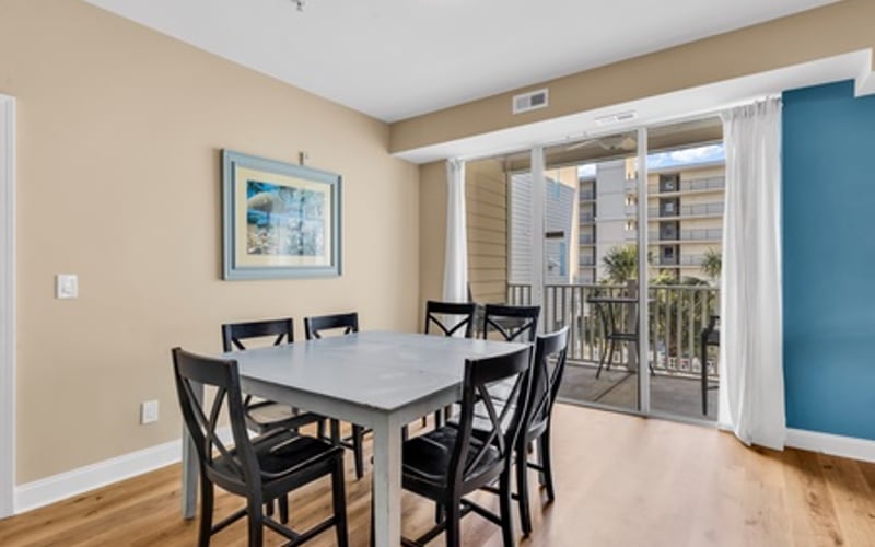 Dining room with gray table, black chairs, and glass doors opening to a balcony with ocean view
