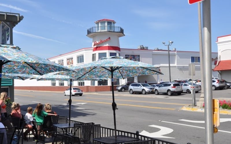 Outdoor patio seating with umbrellas overlooking a street and red-and-white lighthouse-style building