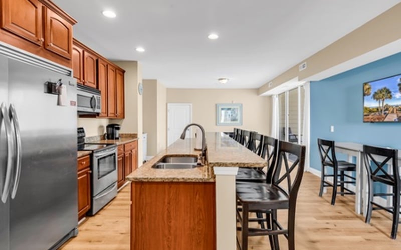 Open-plan kitchen and dining area with wood cabinetry, stainless steel appliances, island with sink, and bar seating