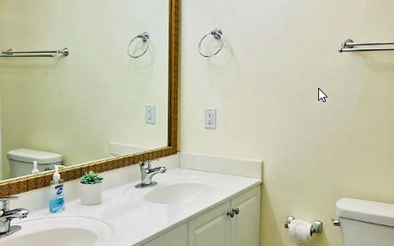Bathroom with pale yellow walls, double vanity with white countertop, large mirror with gold frame, and chrome fixtures