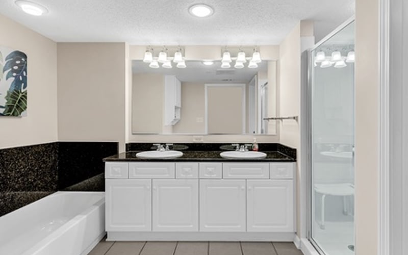 Modern bathroom with white vanity, double sinks, black countertop, soaking tub, and glass shower enclosure