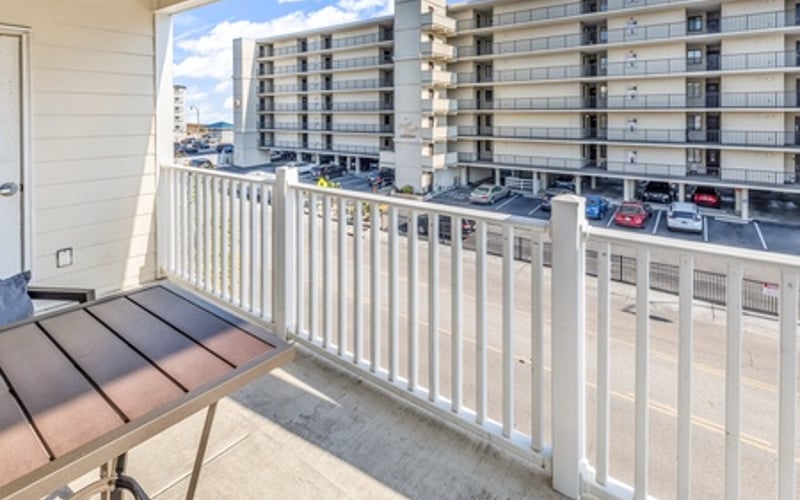 Balcony with white railing overlooking parking lot and multi-story residential building