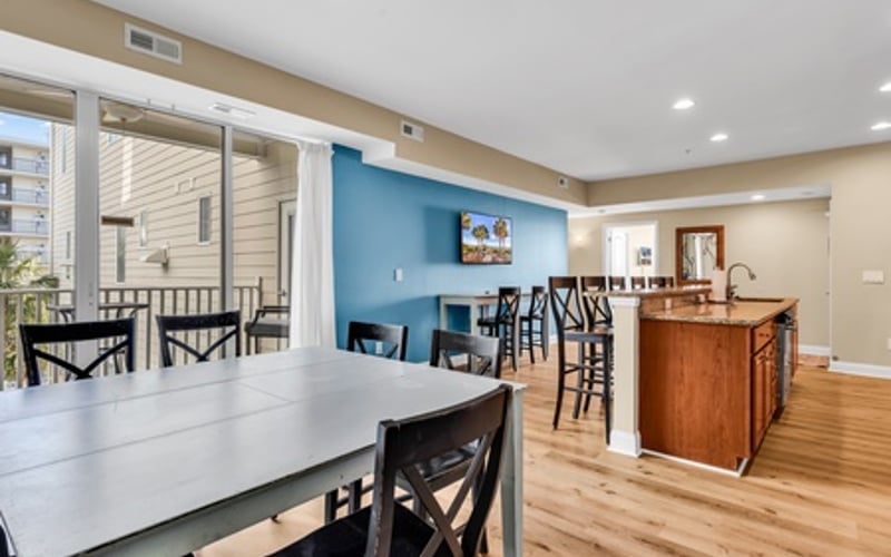 Open-plan kitchen and dining area with white table, black chairs, wooden island, and blue accent wall opening to deck