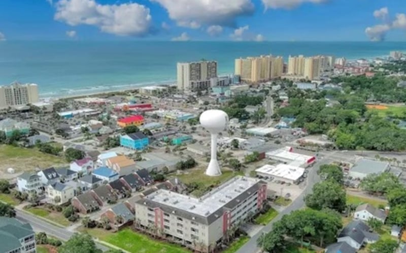 Aerial view of beachfront coastal town with high-rise hotels, water tower, and green residential areas