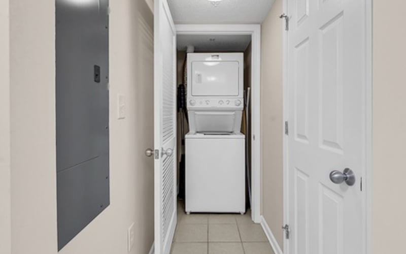 Narrow hallway with stacked washer and dryer unit, white doors, and tile flooring