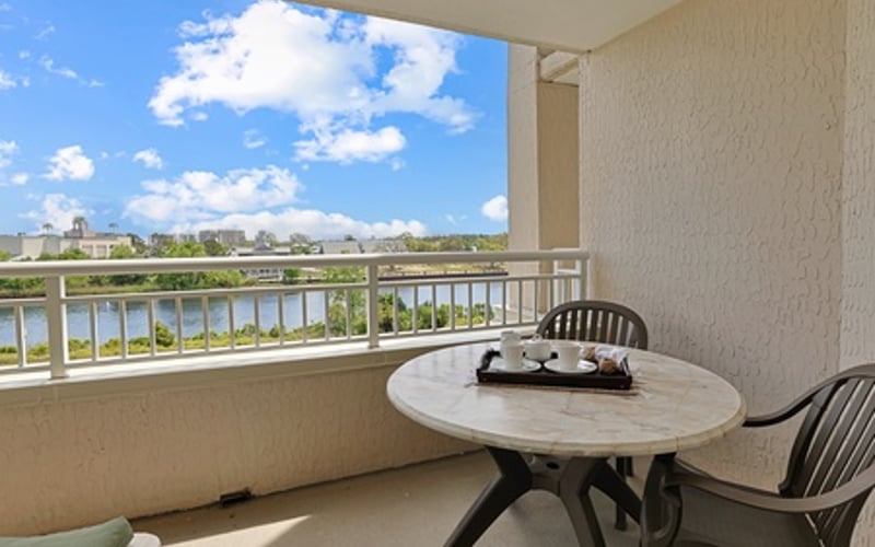 Balcony with round table and chairs overlooking river and distant buildings under blue sky