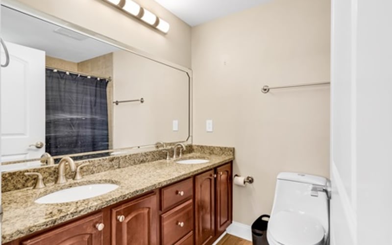 Bathroom with granite countertop, wooden vanity cabinet, dual sinks, and toilet