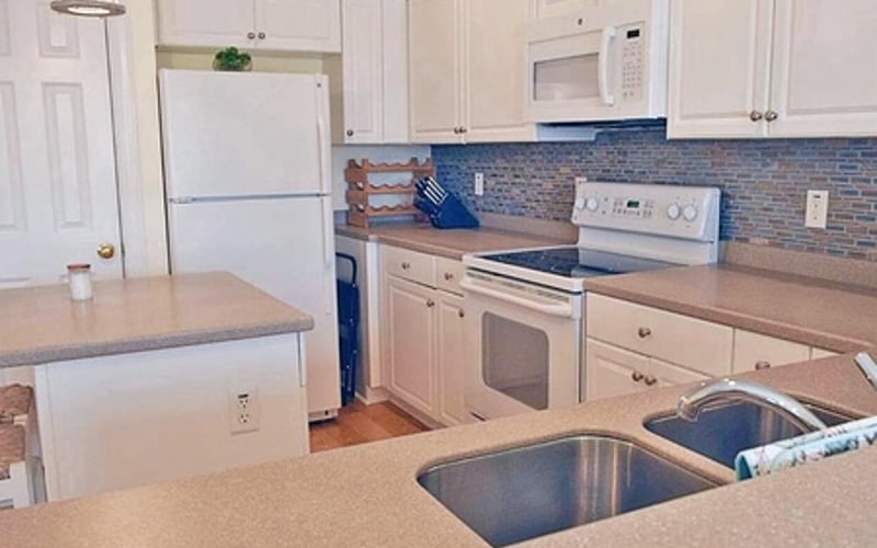 Small kitchen with white cabinets, blue tile backsplash, beige countertops, and stainless steel sink