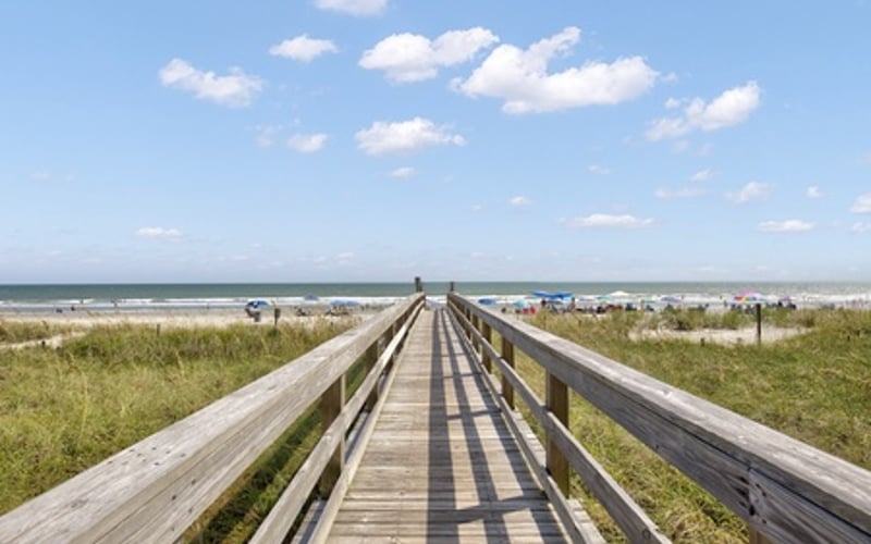 Wooden boardwalk extending toward beach with ocean and dunes visible in distance