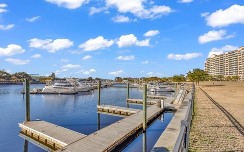 Waterfront marina with wooden docks, moored boats, and high-rise building under blue sky