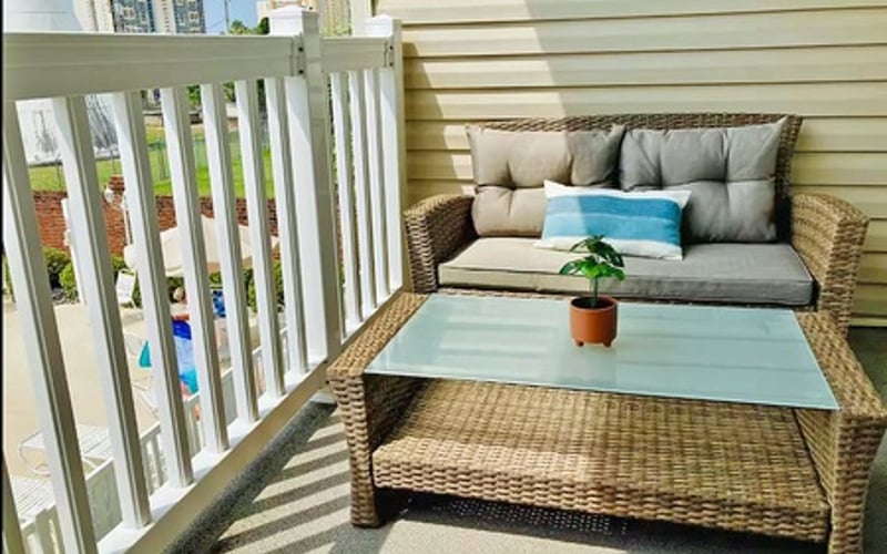 Balcony with wicker seating, gray cushions, glass coffee table, and potted plant overlooking city skyline
